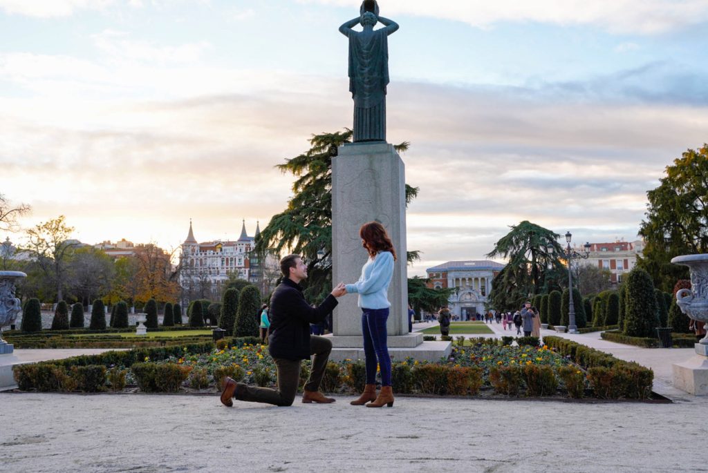 Pareja en la Plaza Parterre del Parque del Retiro durante una pedida de mano, rodeados de jardines románticos